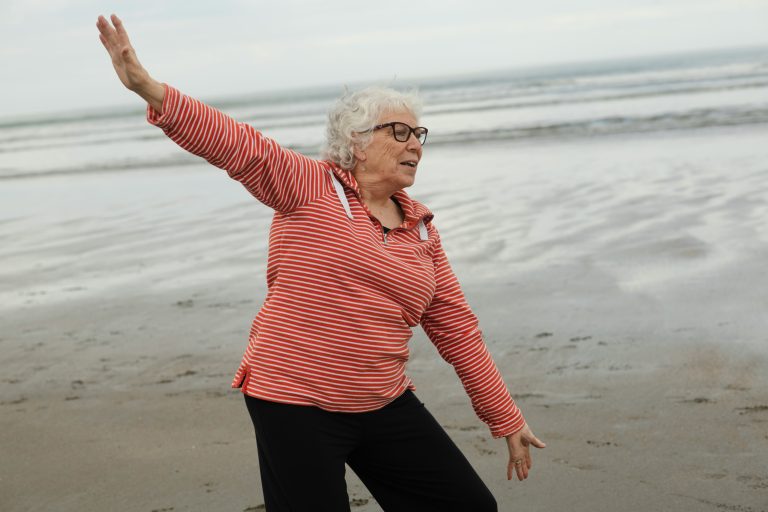 Elderly women stretching on the beach near water.