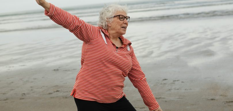 Elderly women stretching on the beach near water.