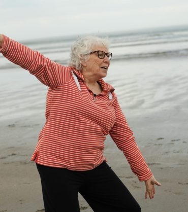 Elderly women stretching on the beach near water.