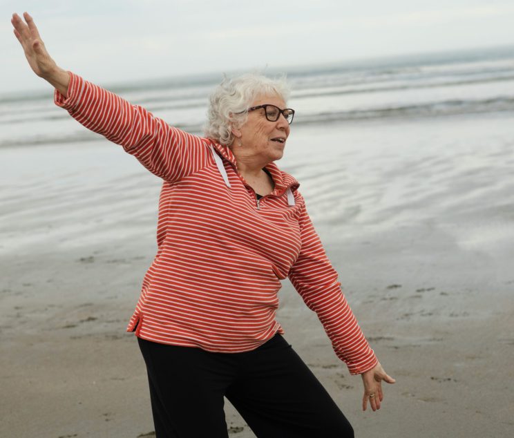 age-cymru-eVTv0dsBgt8-unsplash Elderly women stretching on the beach near water.