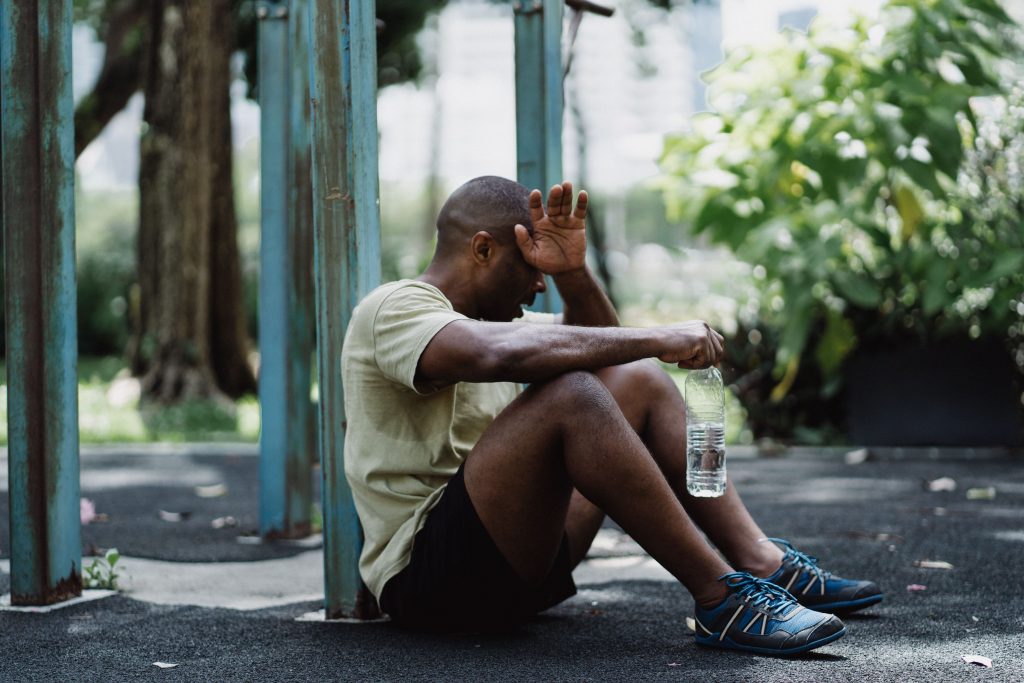 Exhausted man sitting against a pole while holding a water bottle