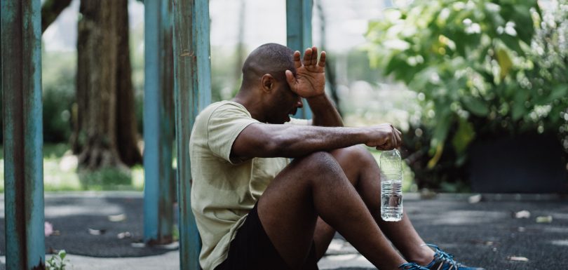 Exhausted man sitting against a pole while holding a water bottle