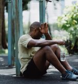 Exhausted man sitting against a pole while holding a water bottle